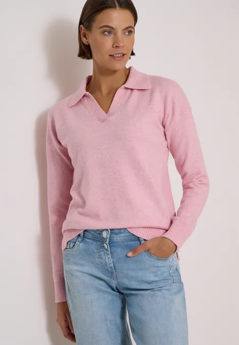 Trui met lange mouwen en polokraag mellow rose melange Vrouw in roze polo-trui met blauwe jeans voor een witte muur.