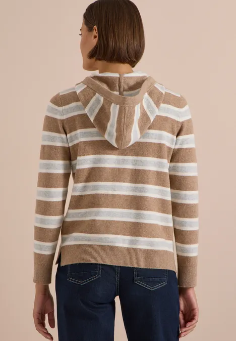 Frau von hinten in gestreiftem Kapuzenpullover in Beige und Weiß, kombiniert mit blauen Jeans.