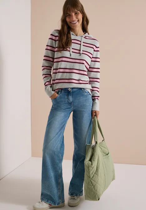 Trui met lange mouwen, capuchon en strepen light grey melange Vrouw met gestreepte hoodie, wijde jeans en grote groene tas, glimlachend voor een lichte achtergrond.