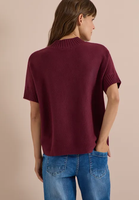 Dolman-trui met col red wine Rückansicht einer Frau in weinrotem Kurzarm-Strickpullover und Jeans vor beigem Hintergrund.