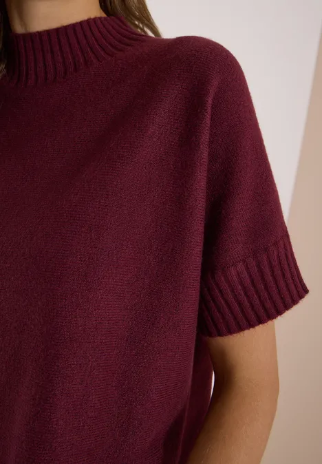 Dolman-trui met col red wine Nahaufnahme einer Person in bordeauxrotem Kurzarm-Strickpullover vor neutralem Hintergrund.
