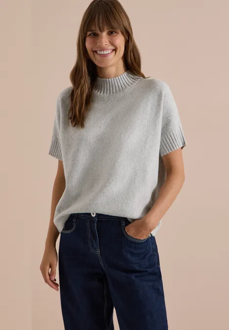 Dolman-trui met col light grey melange Eine lächelnde Frau in grauem Kurzarm-Strickpullover und blauen Jeans.