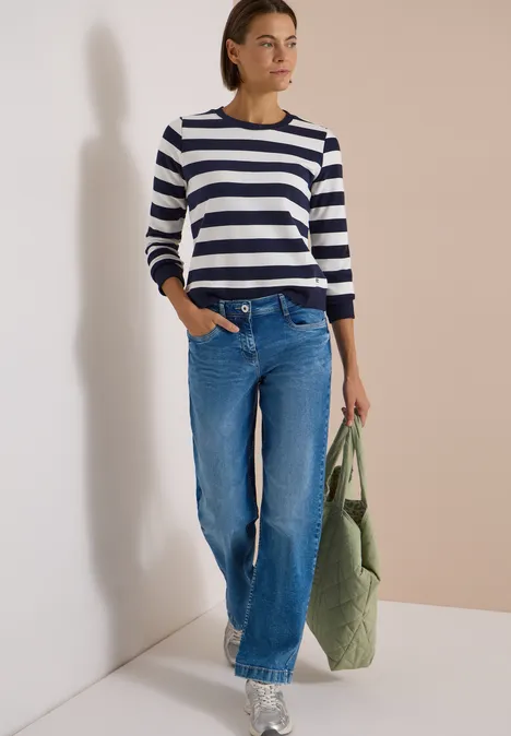 Sweatshirt mit Rundhals und Streifen urban dark blue Frau trägt gestreiften Pullover, weite Jeans und hält eine grüne, gesteppte Stofftasche vor neutralem Hintergrund.