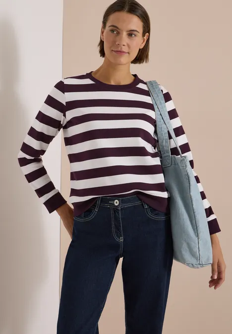 Sweatshirt mit Rundhals und Streifen eggplant red Frau in burgund-weiß gestreiftem Langarmshirt, Jeans und mit hellblauer Jeans-Tasche vor hellem Wandhintergrund.