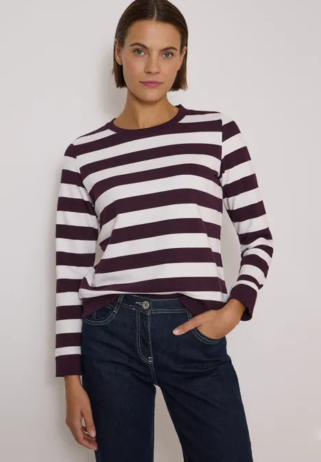 Sweatshirt mit Rundhals und Streifen eggplant red Frau in weiß-dunkel gestreiftem Pullover und Jeans vor hellem Hintergrund.
