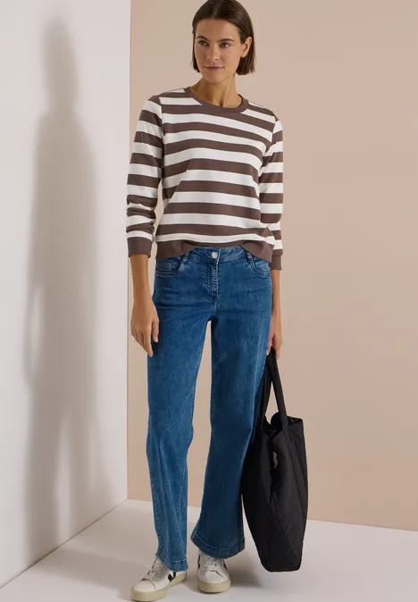 Sweatshirt mit Rundhals und Streifen urban taupe Frau in gestreiftem Pullover, Jeans und schwarzer Tasche steht vor beigem Hintergrund.