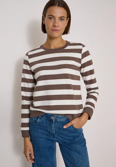 Sweatshirt mit Rundhals und Streifen urban taupe Frau in braun-weiß gestreiftem Langarmshirt und Jeans steht vor hellem Hintergrund.