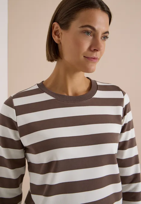 Sweatshirt mit Rundhals und Streifen urban taupe Frau trägt ein braun-weiß gestreiftes Langarmshirt, helles Studio-Setting, leicht lächelnd, kurze Haare.