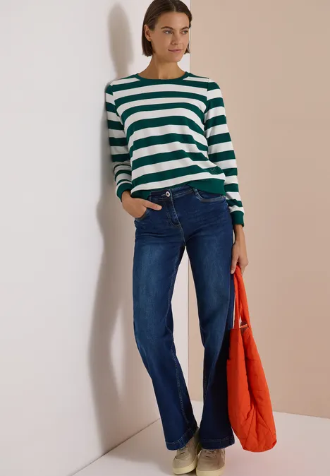 Sweatshirt mit Rundhals und Streifen dark fir green Frau lehnt an Wand, trägt grün-weiß gestreiften Pullover, blaue Jeans und hält rote Tasche.