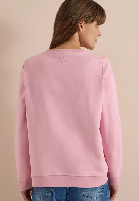 Rückenansicht einer Frau in einem rosa Pullover vor beigem Hintergrund.