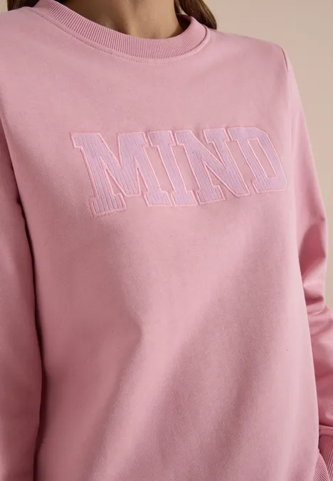 Ein pinkes Sweatshirt mit dem Aufdruck 'MIND' in pastellfarbener Kontur.