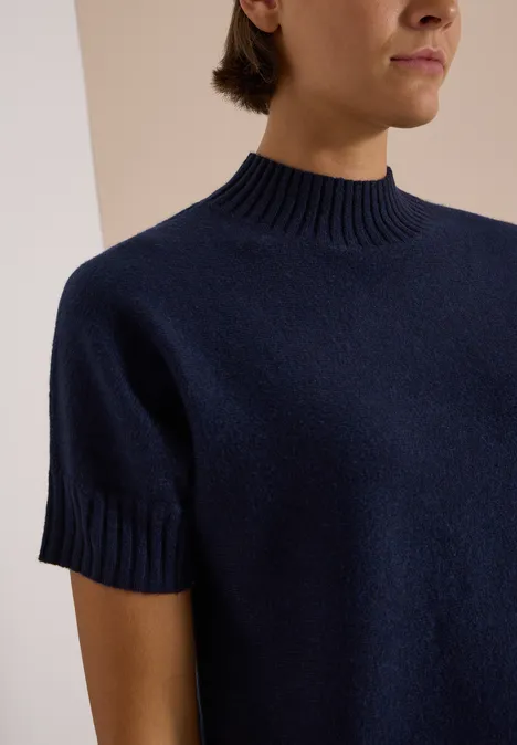 Eine Person trägt einen marineblauen Kurzarmpullover mit hohem Rundhalsausschnitt.