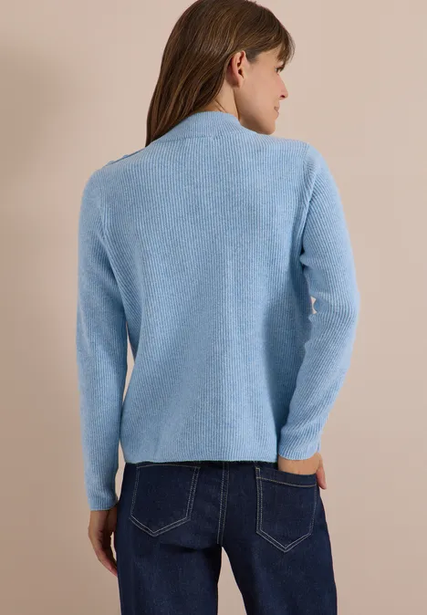 Pullover mit Struktur und Knopfdetail easy blue melange Frau von hinten in einer hellblauen Strickjacke und Jeans vor beigem Hintergrund.