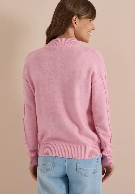 Frau von hinten in rosa Pullover und blauer Jeans vor beigem Hintergrund.