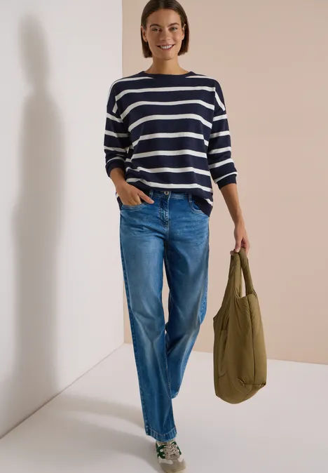 Frau trägt blau-weiß gestreiften Pullover, lockere Jeans und hält olivefarbene Tasche.