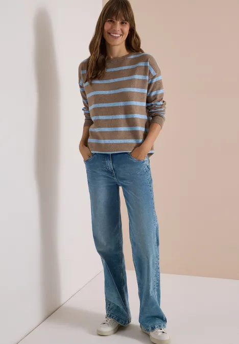 Pullover mit Boat Neck und Streifen urban taupe melange Eine junge Frau in gestreiftem Pullover, blauen Jeans und Sneakers steht lächelnd vor neutralem Hintergrund.