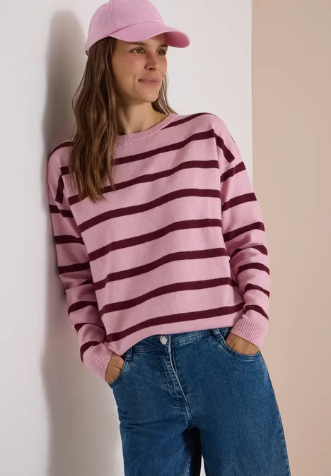 Pullover mit Boat Neck und Streifen mellow rose melange Frau in rosa-lila gestreiftem Pullover, Jeans und rosa Cap lehnt entspannt an der Wand.