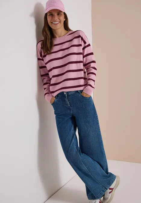 Pullover mit Boat Neck und Streifen mellow rose melange Frau lehnt lächelnd an Wand, trägt rosa Mütze, gestreiften Pullover, weite Jeans und weiße Sneaker.