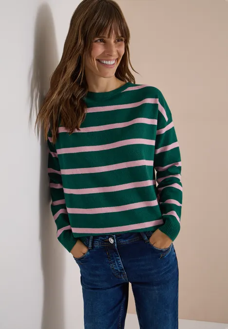 Pullover mit Boat Neck und Streifen dark fir green melange Frau lehnt lächelnd an Wand, trägt grün-rosa gestreiften Pullover und blaue Jeans.