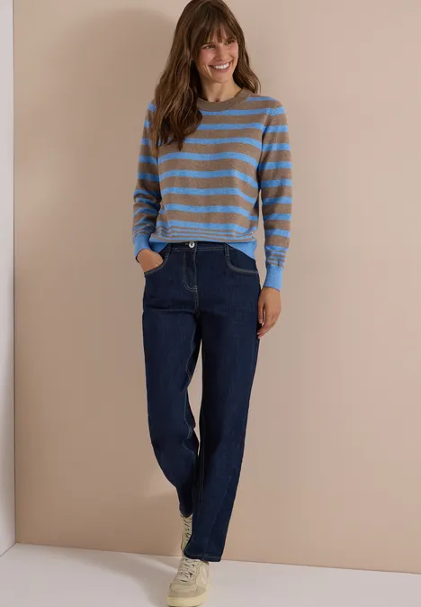 Pullover mit Rundhals und Streifen urban taupe melange Frau in gestreiftem Pullover und Jeans vor beiger Wand, lässiger Look, Hände in den Taschen, weiße Sneaker.