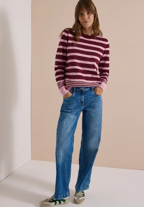 Pullover mit Rundhals und Streifen red wine melange Frau mit gestreiftem Pullover und blauen Jeans steht entspannt mit Händen in den Taschen vor neutralem Hintergrund.