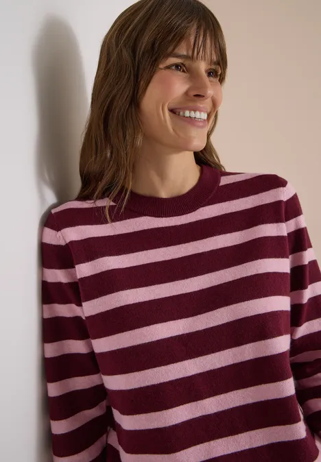 Pullover mit Rundhals und Streifen red wine melange Lächelnde Frau lehnt an Wand und trägt einen gestreiften Pullover in Dunkelrot und Rosa.