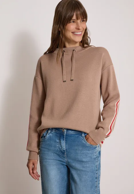 Trui met col en college-details creamy mocha melange Vrouw in beige hoodie met strepen op de mouwen en blauwe jeans, glimlachend.