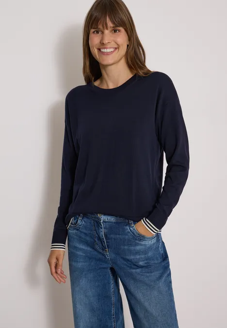 Pullover mit Rundhals und Layering-Detail urban dark blue Frau in dunkelblauem Pullover mit gestreiften Manschetten und Jeans posiert vor hellem Hintergrund.
