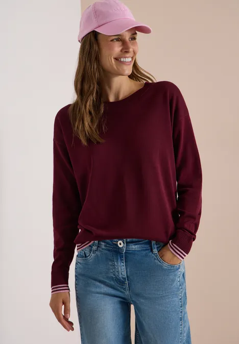 Pullover mit Rundhals und Layering-Detail red wine Eine junge Frau mit pinker Cap, bordeauxrotem Langarmshirt und Jeans lächelt entspannt.