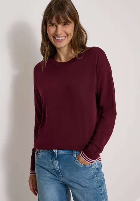 Pullover mit Rundhals und Layering-Detail red wine Lächelnde Frau in weinrotem Langarmshirt und Jeans vor hellem Hintergrund.