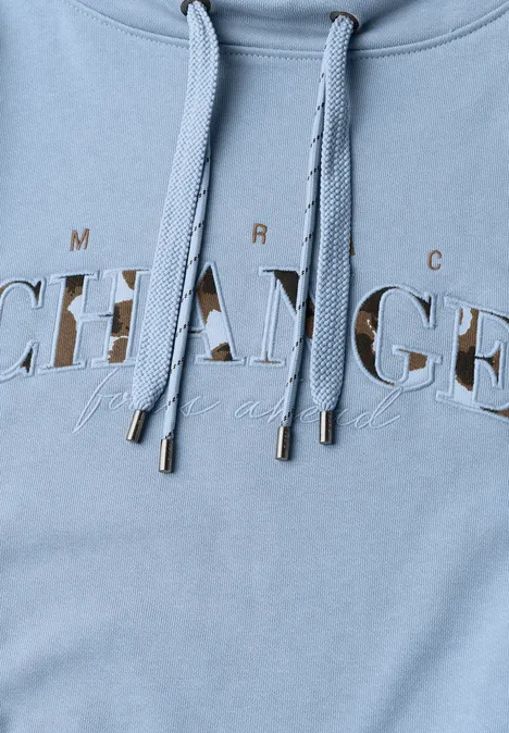 Hellblauer Hoodie mit Kordeln und Metallenden, bedruckt mit dem Schriftzug 'CHANGE' und kleinem Untertext.