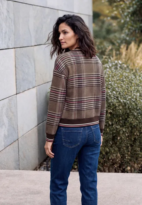 Sweat-shirt à col rond et motif à carreaux dark toffee brown Eine Frau in karierter Jacke und Jeans lehnt an einer Steinmauer und blickt zurück.