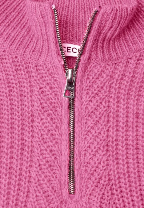Nahaufnahme eines rosa Strickpullovers mit Zopfmuster und silbernem Reißverschluss.