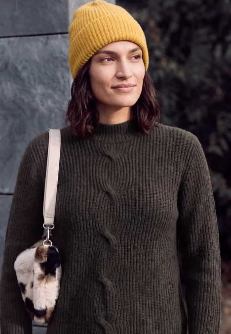 Frau mit gelber Strickmütze und dunkelgrünem Pullover, trägt eine kleine Felltasche.
