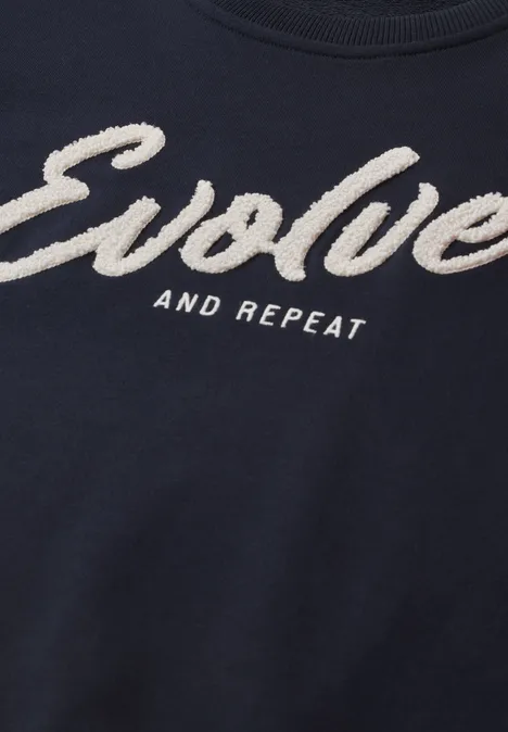 Sweatshirt mit Rundhals und Wording urban dark blue Dunkelblaues T-Shirt mit weißem Schriftzug "Evolve and Repeat" in auffälliger, flauschiger Schrift.