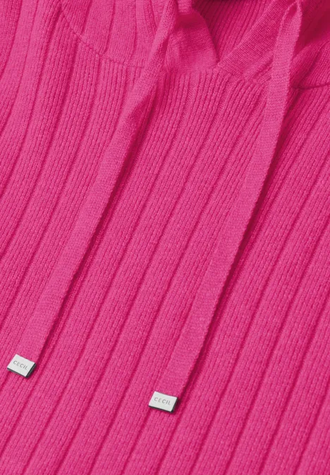 Zbliżenie na różowy sweter typu hoodie z kapturem i sznurkami zakończonymi metalowymi końcówkami.