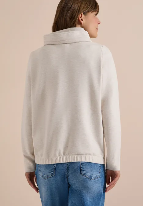 Frau von hinten in kremfarbenem Strickjacke mit breitem Kragen und blauen Jeans.