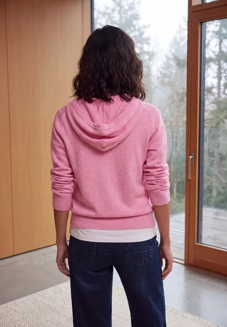 Pull uni à capuche dark blossom melange Femme vue de dos en sweat à capuche rose et jeans devant de grandes fenêtres