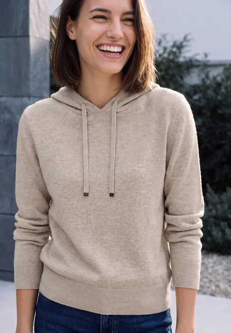 Pull uni à capuche Coffee beige melange Une femme souriante en sweat à capuche beige devant un fond flou.