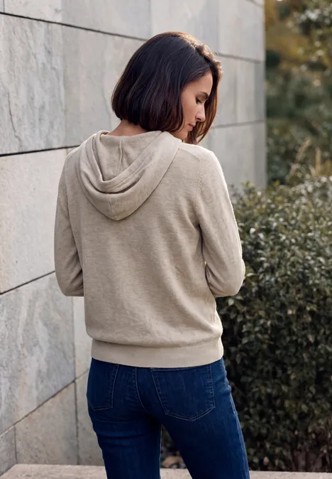 Pull uni à capuche Coffee beige melange Jeune femme en sweat à capuche beige et jean appuyée sur un mur de pierre à l'extérieur.