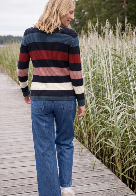 Rückansicht einer Frau in gestreiftem Pullover und Jeans auf einem Steg am Schilf.