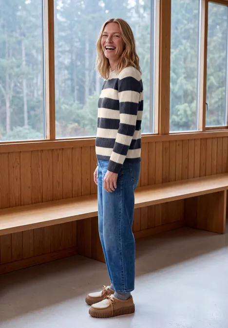 Pullover mit Turtle Neck und Streifen urban dark blue Eine lächelnde Frau in gestreiftem Pullover und Jeans vor Fenstern und Holzverkleidung.