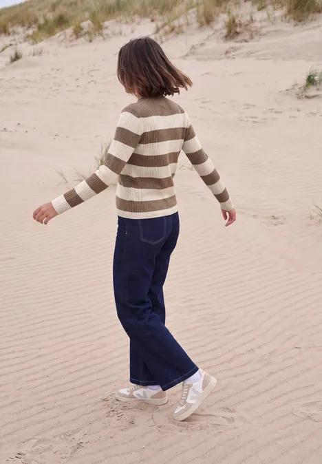 Pullover mit Turtle Neck und Streifen creamy mocha melange Eine junge Frau mit gestreiftem Pullover und dunkler Jeans spaziert über Sanddünen am Strand.