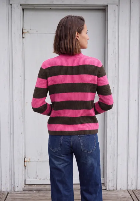 Pullover mit Turtle Neck und Streifen pink flash Eine Frau steht mit dem Rücken zur Kamera, trägt einen pink-braunen Ringelpullover und blaue Jeans.