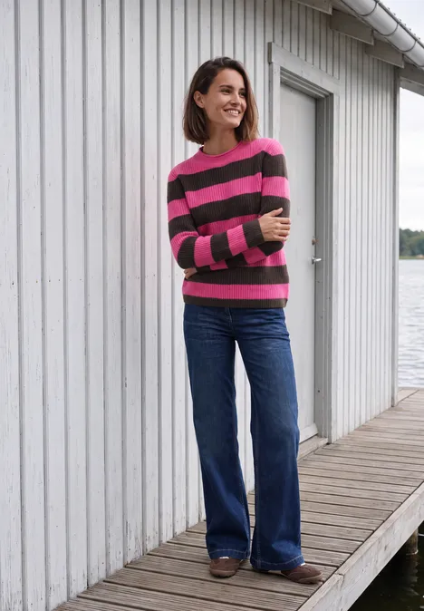 Pullover mit Turtle Neck und Streifen pink flash Eine Frau in gestreiftem Pullover und weitem Jeans steht auf einem Steg vor einem weißen Haus mit Fenster.