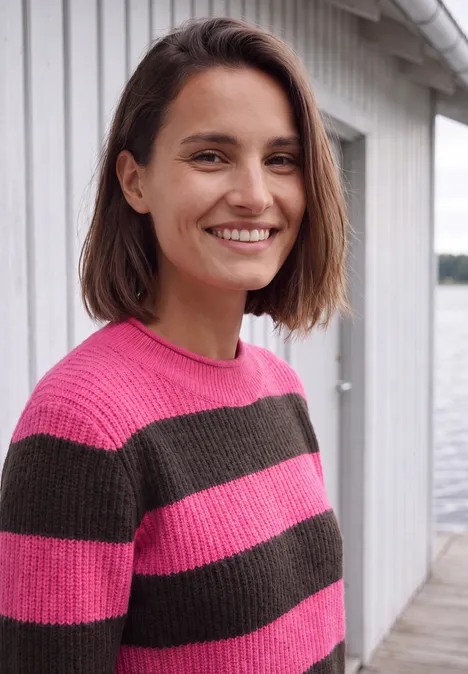 Pullover mit Turtle Neck und Streifen pink flash Eine Frau mit kurzem braunem Haar lächelt in einem pink-grau gestreiften Pullover vor hellem Hintergrund.