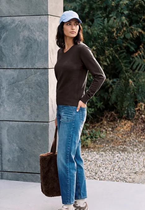 Une jeune femme en jean, pull noir et casquette, portant un sac, regard latéral.