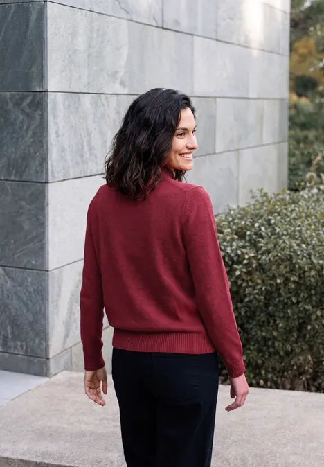 Pullover in Unifarbe mit Turtle Neck rhubarb melange Frau im roten Pullover steht an einer Wand und schaut über die Schulter.