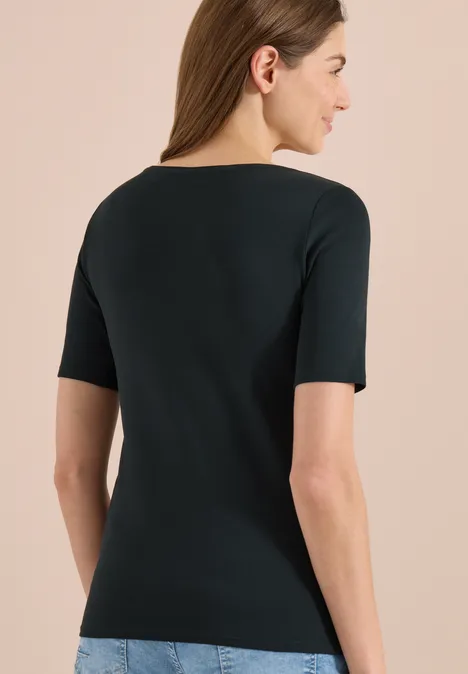 Achteraanzicht van een vrouw in een zwart topje met korte mouwen en een blauwe spijkerbroek voor een lichte achtergrond.