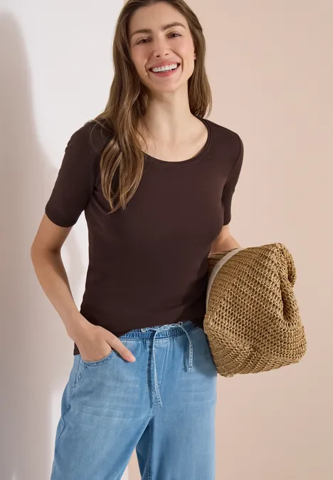 Femme en t-shirt marron et jean tient un sac tricoté beige clair et texturé.